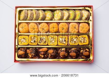 stock photo of Indian sweet or mithai and oil lamp or diya with gift box and flowers on decorative or colourful background, selective focus