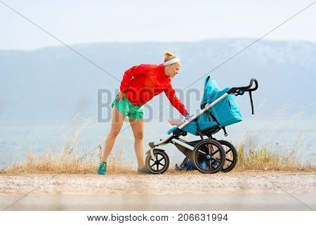 Mother with child in stroller enjoying motherhood at sunset and mountains landscape. Jogging or power walking woman with pram at sunset. Beautiful inspirational mountains landscape.