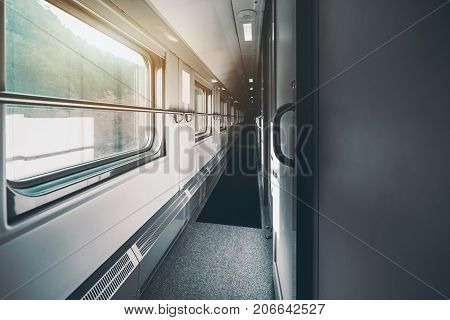 Wide-angle shooting of long and empty double-decker passenger train interior with multiple closed doors of compartments hills outside the windows carpet on the floor railings on the walls