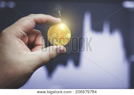 Man hand holding golden Bitcoin on forex chart background, selective focus, toned