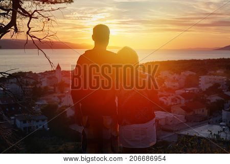 Sensual portrait profile of silhouette romantic adult couple admiring sunset with picturesque view to the Croatian town Makarska. Two travelers enjoying city view ladscape from the top of hill.