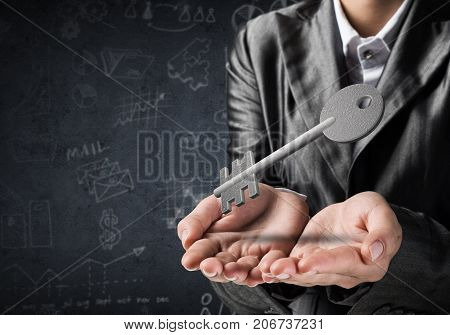 Cropped image of businessman in suit keeping stone key symbol in hands with business sketches on dark wall on background. 3D rendering.