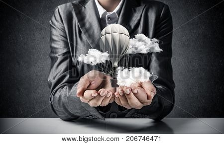 Closeup of business woman in suit presenting flying aerostate among clouds in her palms with dark wall on background. 3D rendering.