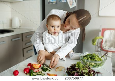 Beautiful dark haired mother cooking dinner in front of her adorable little son. Child looking aside with amezed expression