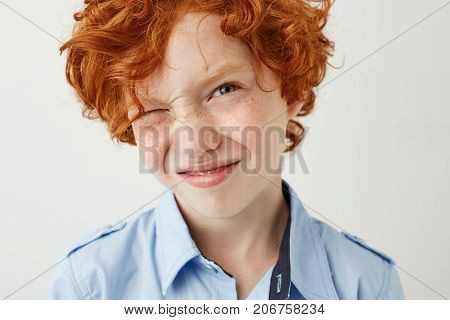 Close up of funny ginger boy with freckles and red cheeks screw up eye because of bright lightning in school class