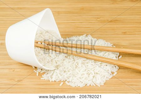 White Rice Spill Out Of Wite Ceramic Bowl With Two Bamboo Sticks