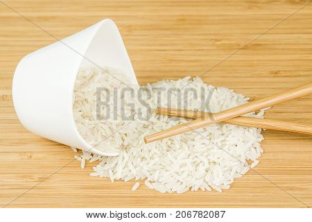 White Rice Spill Out Of Wite Ceramic Bowl With Two Bamboo Sticks