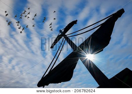 Silhouette of a mast of a pirate ship with midday sun shining over blue sky background