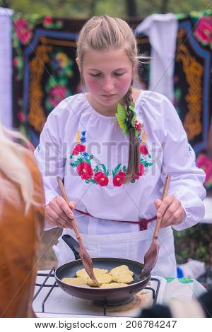 Korosten Ukraine - September 06 2016: ukrainian traditional food outdoors open kitchen young woman pouring oil into frying potato pancakes.
