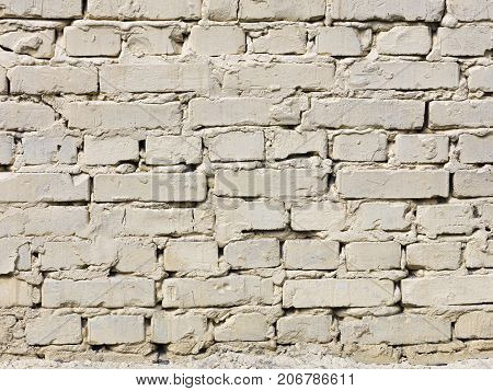 The texture of a very old brick wall is painted with light beige paint and is illuminated by daylight