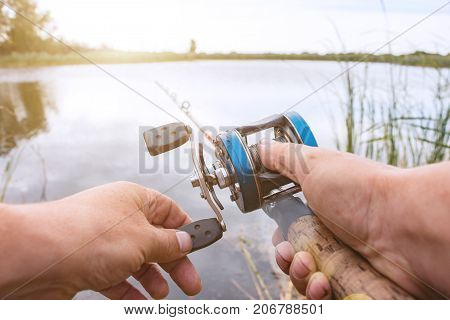 A man is fishing with a backcasting reel. Hands, a rod and a backcasting reel in the background of the rising sun