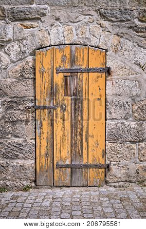 Old weathered orange wooden door in stone wall