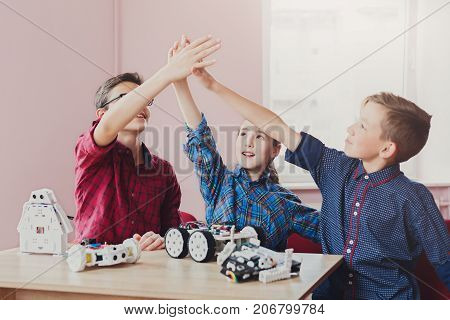 Successful teamwork. Children giving group high-five after creating robots at school, stem education. Early development, diy, innovation, modern technology concept