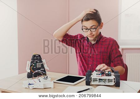 Stem education. Embarrassed boy made mistake while creating robot at lab, looking at blank tablet screen. Early development, diy, innovation, modern technology concept