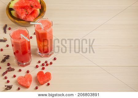 Two hearts, watermelon juice in two glass glasses with a straw on a light wooden background, a delicious cocktail, a wooden plate with slices of ripe red watermelon on the table with berries cranberries and watermelon seeds