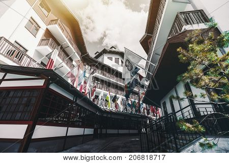 Wide-angle view from bottom of small street with multiple national flags of different countries fixed to facades of wooden houses sunny summer day Sochi Russia