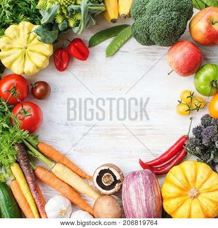 Colorful frame made of fresh raw vegetables, fruits herbs on white wooden background, copy space for text in the middle, top view, square, selective focus
