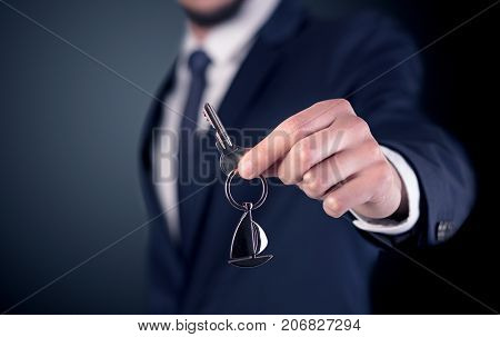 Young businessman hand over keys with empty dark background
