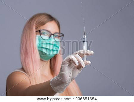 Doctor or nurse in face mask holding syringe isolated over gray