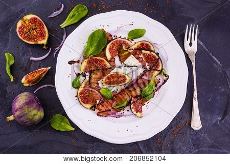 Figs and fried bacon with small lettuce leaves served on a white plate. Italian food.