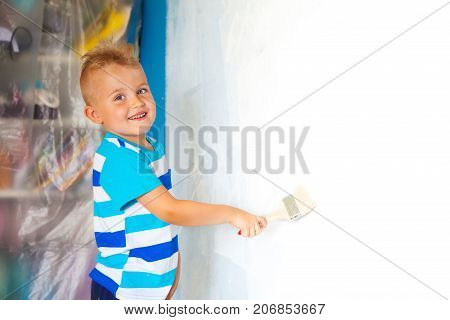 The Child Paints The Blue Wall With A Roller. The Boy Holds A Large Brush For Painting. Home Repairs