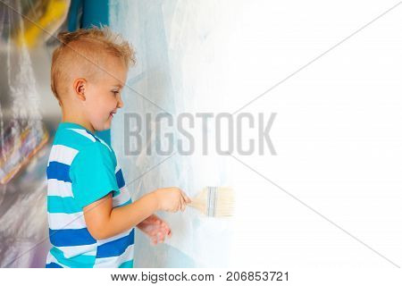 The Child Paints The Blue Wall With A Roller. The Boy Holds A Large Brush For Painting. Home Repairs