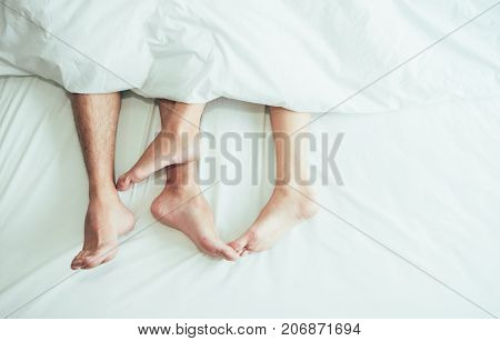The feet or foot of couples sleeping on the bed and cover by the white blanket on a bright Sunday morning.