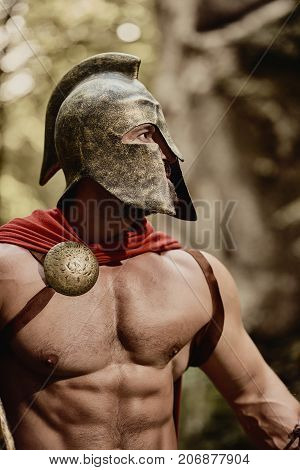 Anonymous man with muscular body posing shirtless in gladiator helmet and red cloak looking pensively away. Spartan.
