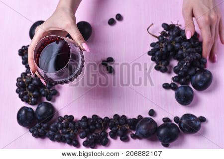 composition of wine, grape and plums on a pink background