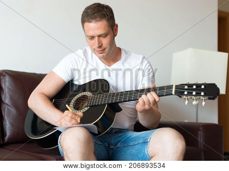 Handsome man compose a song on the guitar.