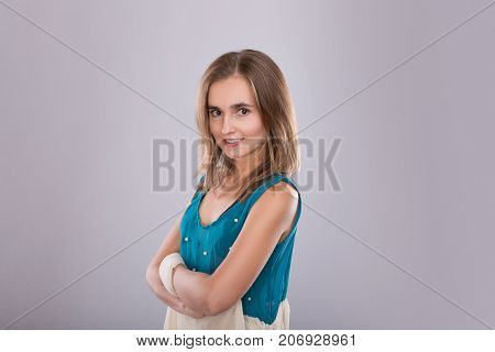 portrait of a smiling teen girl wearing a blue dress and standing with her hands near the heart. Concept of romance and love. Gray background. Studio shooot