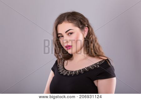 Portrait of a plus size female model posing in black dress over grey background. Beautiful woman with curvy figure.