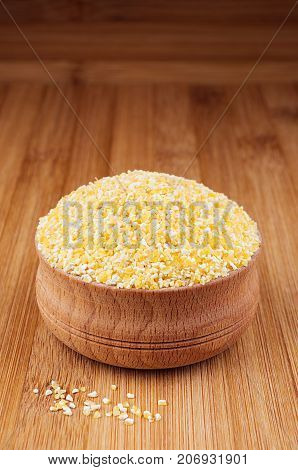 Corn grits in wooden bowl on brown bamboo board closeup. Rustic style healthy dietary groats background.