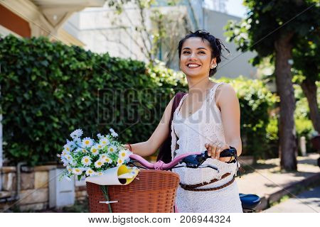 Relaxing summer woman smiling,holds bike with flowers chamomile in backet