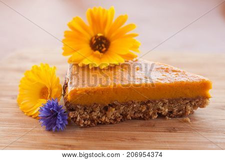 Little piece of tasty home made pumpkin pie on a bamboo desk served with gaden flowers.