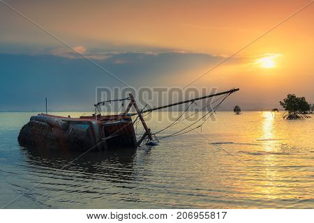 An old shipwreck or abandoned shipwreck Boat capsized on beach in beautiful sunset background Thailand.