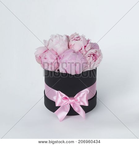 Luxury beautiful pink bouquet of peony flowers round black box with bow on gray background