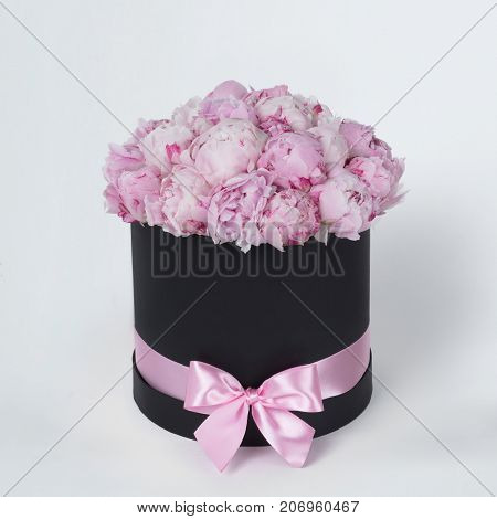 Luxury beautiful pink bouquet of peony flowers round black box with bow on gray background