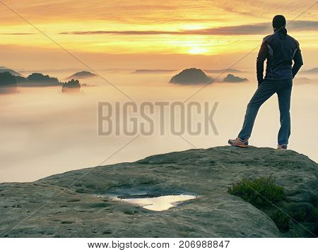Man stands alone on the peak of rock. Hiker watching to autumn Sun at horizon . Beautiful moment the miracle of nature. Colorful mist in valley. Man hike. Person silhouette stand