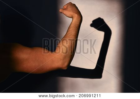 Physical strength and weakness. Strong hand of the sportsman and its reflection on the wall a thin shadow. Expected and reality. Sports achievements and victory