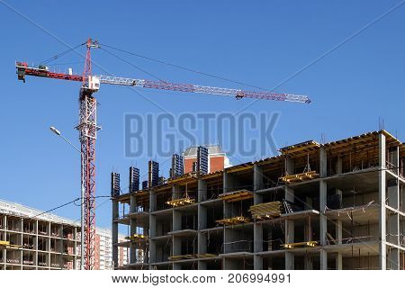 The tower crane builds a concrete house against the blue sky.