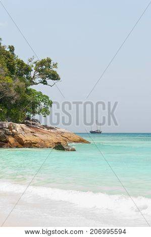 Rocky coastline Andaman sea. White sand on foreground. Crystal clear water and sailboat  on skyline
