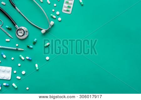 Pills And Medical Equiupments Including Stethoscope, Syringe And Scissors At Border On Green Backgro