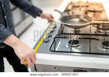 Male Hand Interior Designer Using Tape Measure On Gas Stove On Modern Countertop In Kitchen Showroom