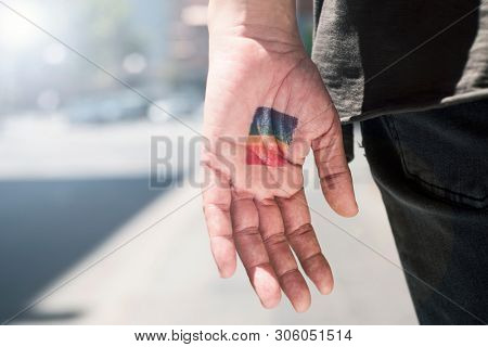 closeup of a rainbow flag in the palm of the hand of a young caucasian person, wearing casual clothing, seen from behind, on the street
