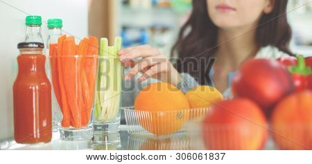 Portrait of female standing near open fridge full of healthy food, vegetables and fruits. Portrait of female