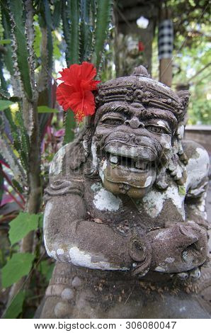 Ubud, Bali, Indonesia - 9th May 2018 : Typical Balinese Dvarapala Stone Statue With A Red Hibiscus F