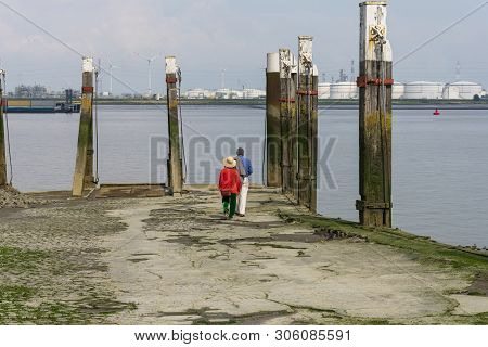 Older Couple Walks On The Quay To The Water To Watch The Ships Sail And Enjoy The Western Scheldt In