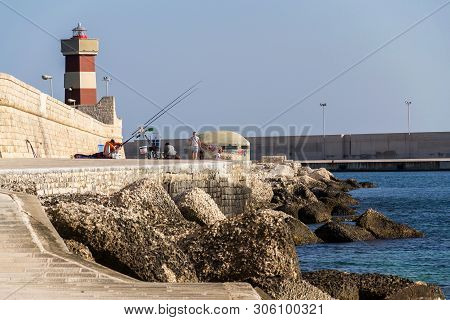 Monopoli, Italy - July 6 2018: Man Fishing In Front Of Lighthouse In Monopoli Port Near Castle Of Ca