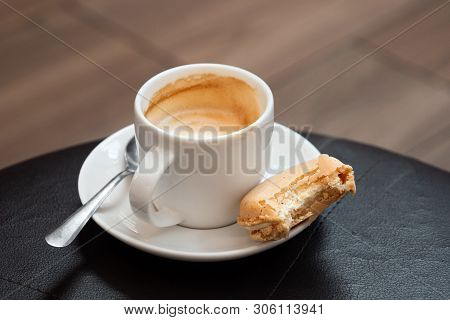 Half Full Cup Of Espresso Macchiato With Metal Spoon And Half Eaten Vanilla Macaron On Saucer. Black
